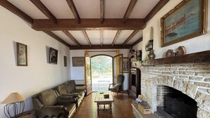Uma sala de estar com lareira de pedra, vigas de madeira, um sofá, uma mesa de centro e um quadro na parede.