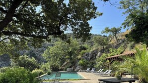 Área de piscina com espreguiçadeiras, mesa e pérgola.