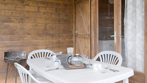 En træhytte med et spisebord dækket til to personer, grill og et køkkenområde, der ses igennem en glasdør.
