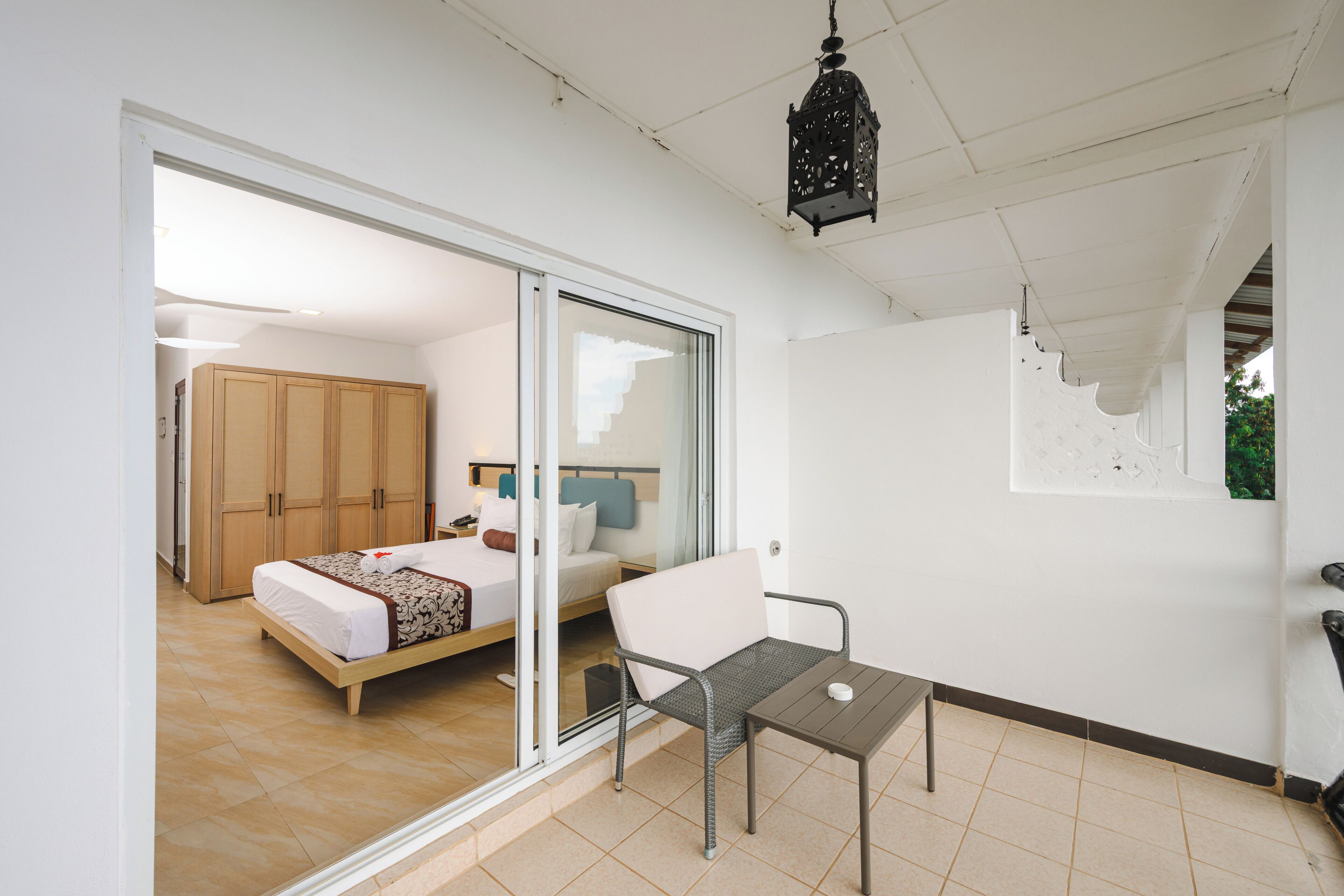 A bedroom with a bed, a chair, a table, and a sliding glass door leading to another room.