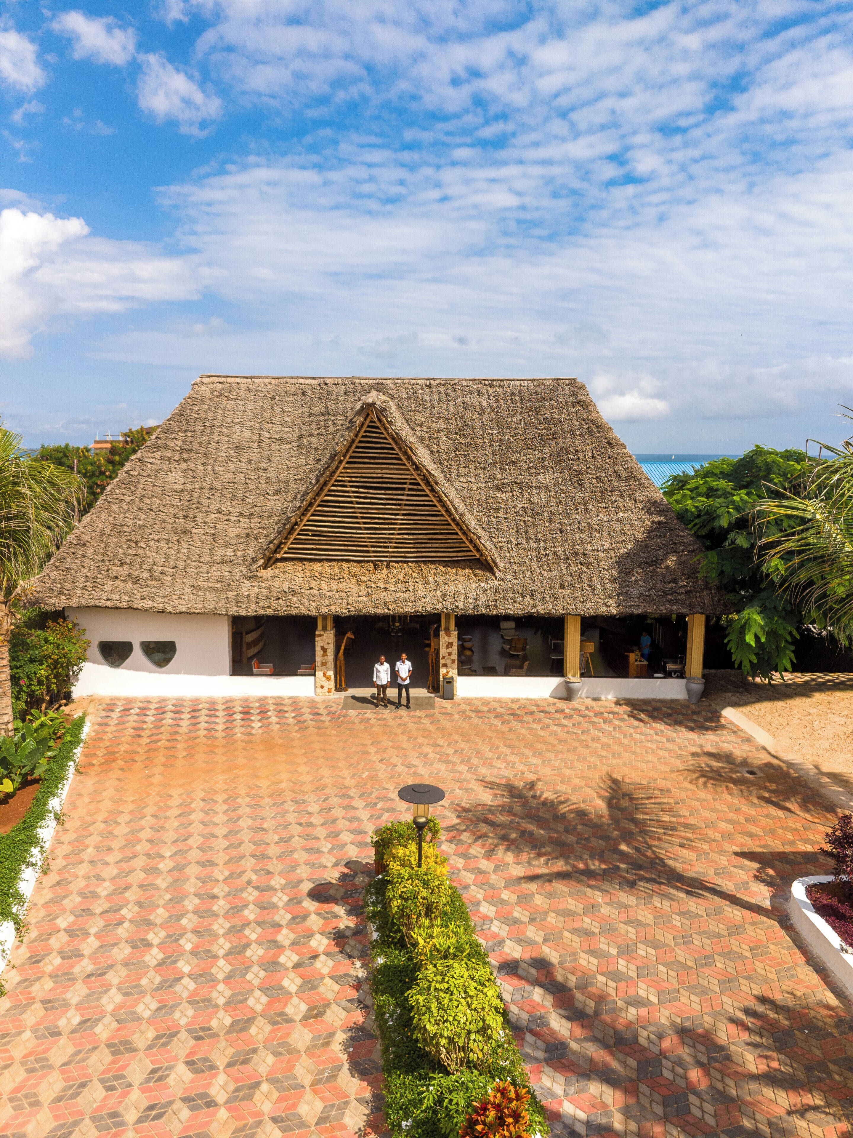 A traditional thatched-roof building with a symmetrical facade, a central entrance, and a paved courtyard with a patterned walkway.