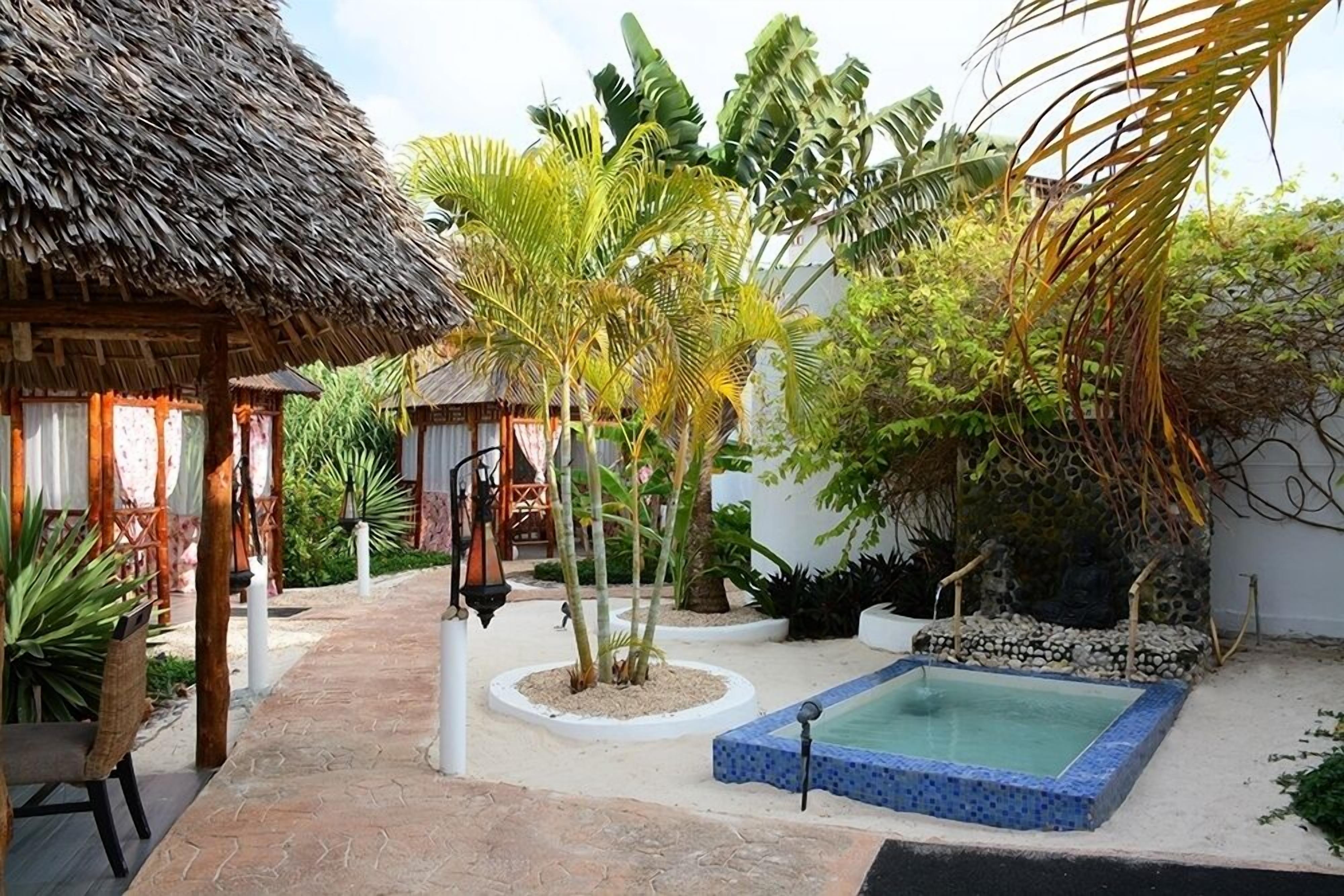 A tropical garden with a pool, a thatched-roof structure, and various plants.