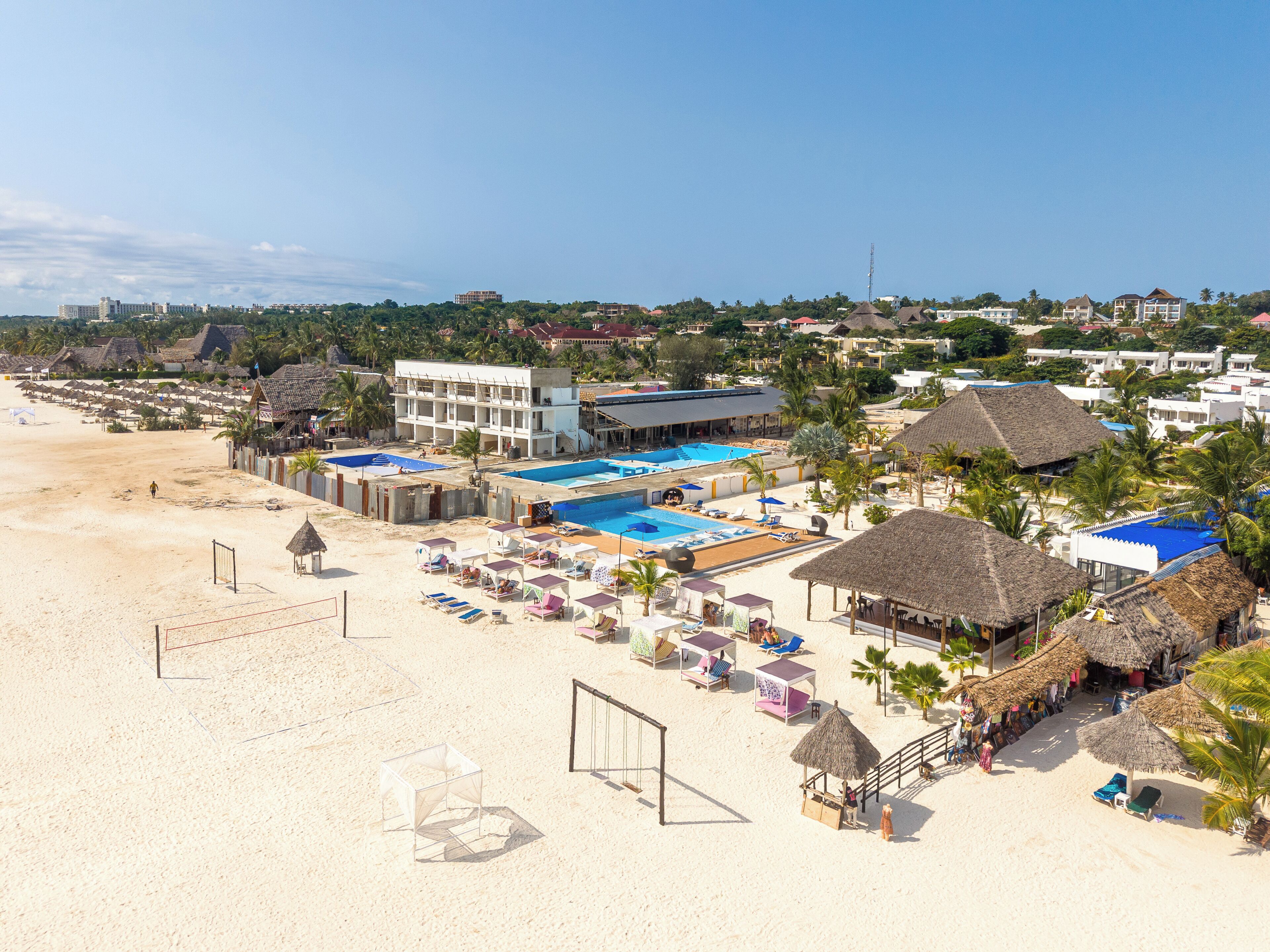 Ett hotell vid stranden med en swimmingpool, parasoller och solstolar.