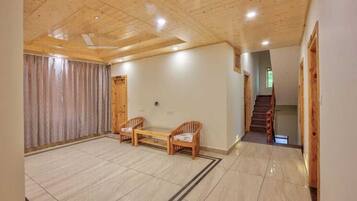 A spacious room with a wooden ceiling, a large window with curtains, a wooden bench, and a staircase leading to another area.