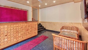 A reception area with a wooden reception desk, a red accent wall, a ceiling fan, and a staircase leading upstairs. - OnlyStay Surya Mall Road Manali (Manali)