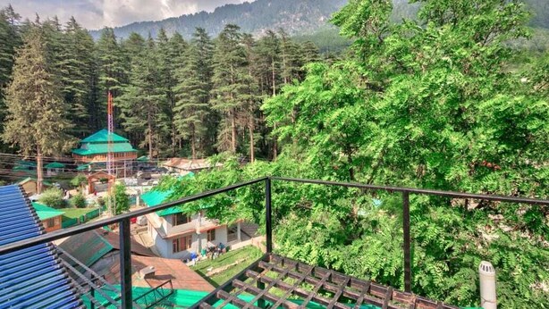 A mountainous landscape with dense forest and a small building with a green roof. - OnlyStay Surya Mall Road Manali (Manali)