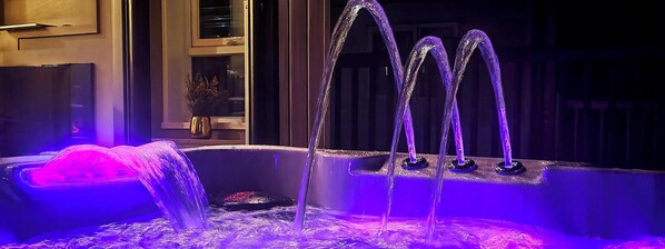 Een jacuzzi met meerdere waterstralen, verlicht met paars licht, en een klein watervalletje.