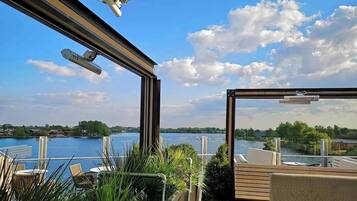 A balcony with a view of a lake, outdoor seating, and a glass railing.