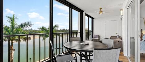 A balcony with a round table and chairs, overlooking a body of water and palm trees.