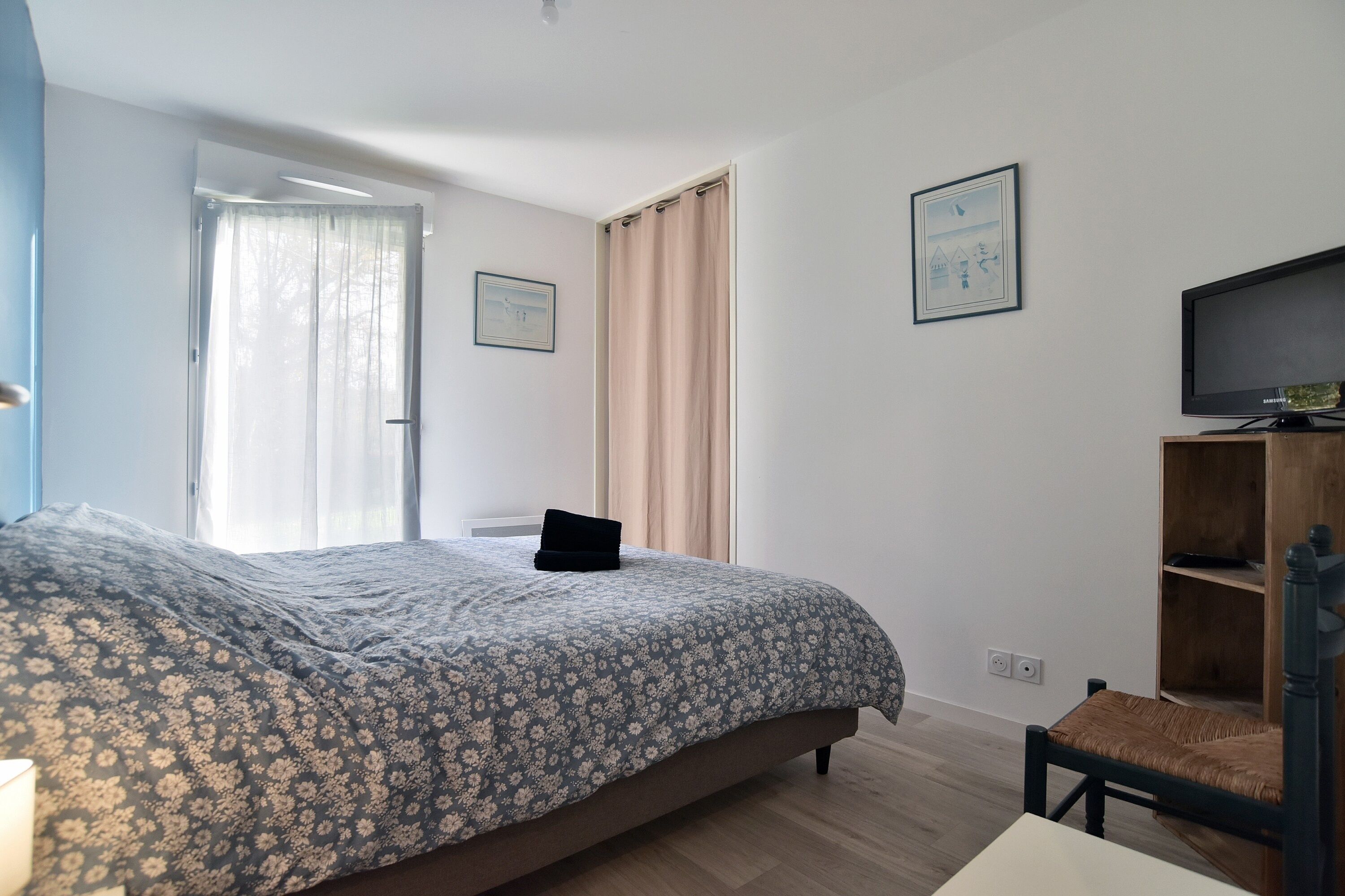 A bedroom with a bed, a chair, a television, and a window with curtains.