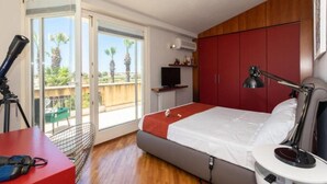 A bedroom with a bed, a desk, a chair, a TV, and a balcony with a view of palm trees. - Family Rooms with Sea View, Private Hot Tub, Wi-Fi and Air Conditioning (Marsala)