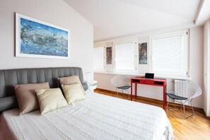 Une chambre à coucher avec un lit, un bureau avec un ordinateur portable, deux chaises et une fenêtre avec des stores.