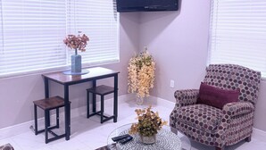 A living room with a flat-screen TV mounted on the wall, a dining table with chairs, a patterned armchair, a round coffee table, and a sofa.