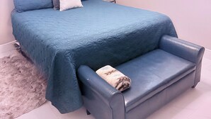 A bedroom with a bed, a bedside table, a lamp, and two windows with blinds.
