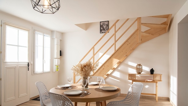 A dining area with a round table, four chairs, and a wooden staircase.