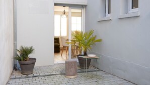 A narrow outdoor space with potted plants, a small round table, and a chair.