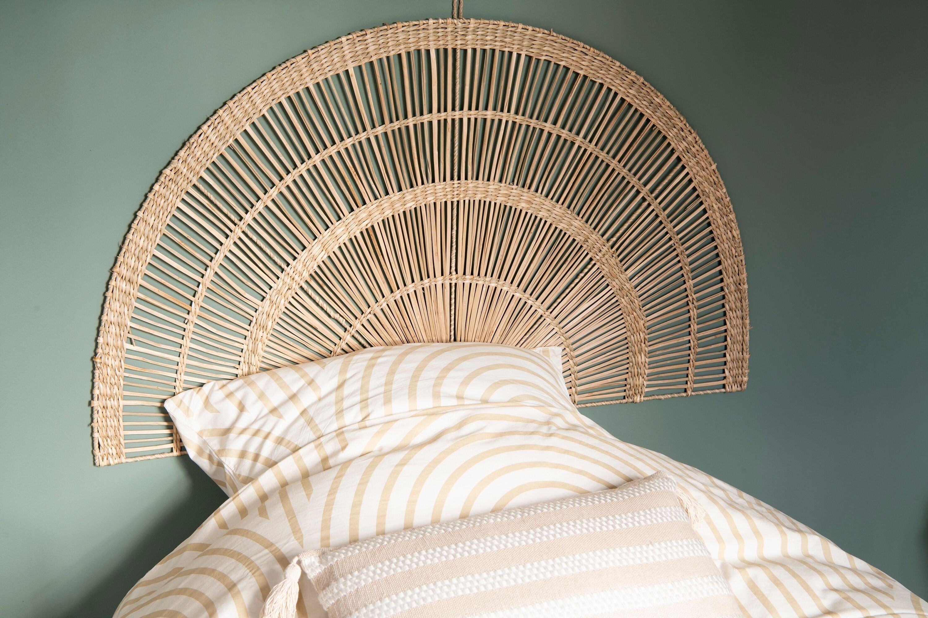 A wicker headboard with a curved design against a teal wall.