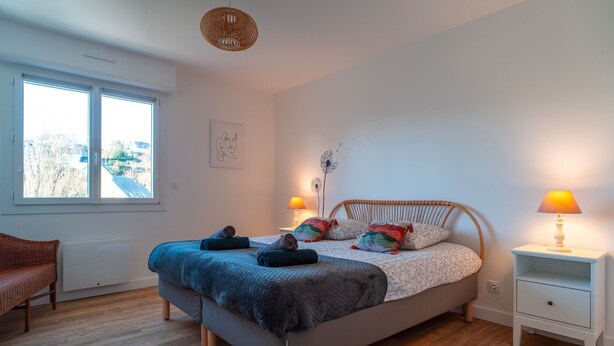 Un dormitorio con cama, lámparas de noche, una silla y una ventana.