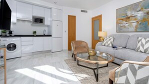 A modern kitchen with built-in appliances, a dining area with a round table, and a living room with a sofa and a painting. - Genteel Home Uceda II (Cordoba)