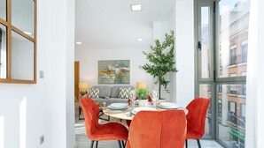 A dining area with a round table, four orange chairs, a potted plant, and a city view through large windows. - Genteel Home Uceda II (Cordoba)
