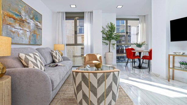 A modern living room with a grey sofa, a glass coffee table, and a red dining set. - Genteel Home Uceda II (Cordoba)