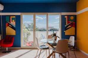 Une pièce moderne avec une table en verre, des chaises, un fauteuil rouge et des œuvres d’art abstraites accrochées au mur.