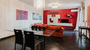 A modern living room with a glass dining table, black chairs, a red sofa, and a white entertainment unit.