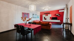 A modern living room with a dining area, a red accent wall, and a chandelier.