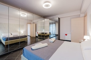 Une chambre d’hôtel moderne avec un grand lit, une table de chevet, un miroir et une salle de bain visible à travers une paroi en verre.
