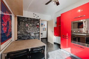 Une cuisine moderne avec des meubles de rangement rouges, un four en acier inoxydable et un mur recouvert d’un tableau noir où sont inscrits des messages.