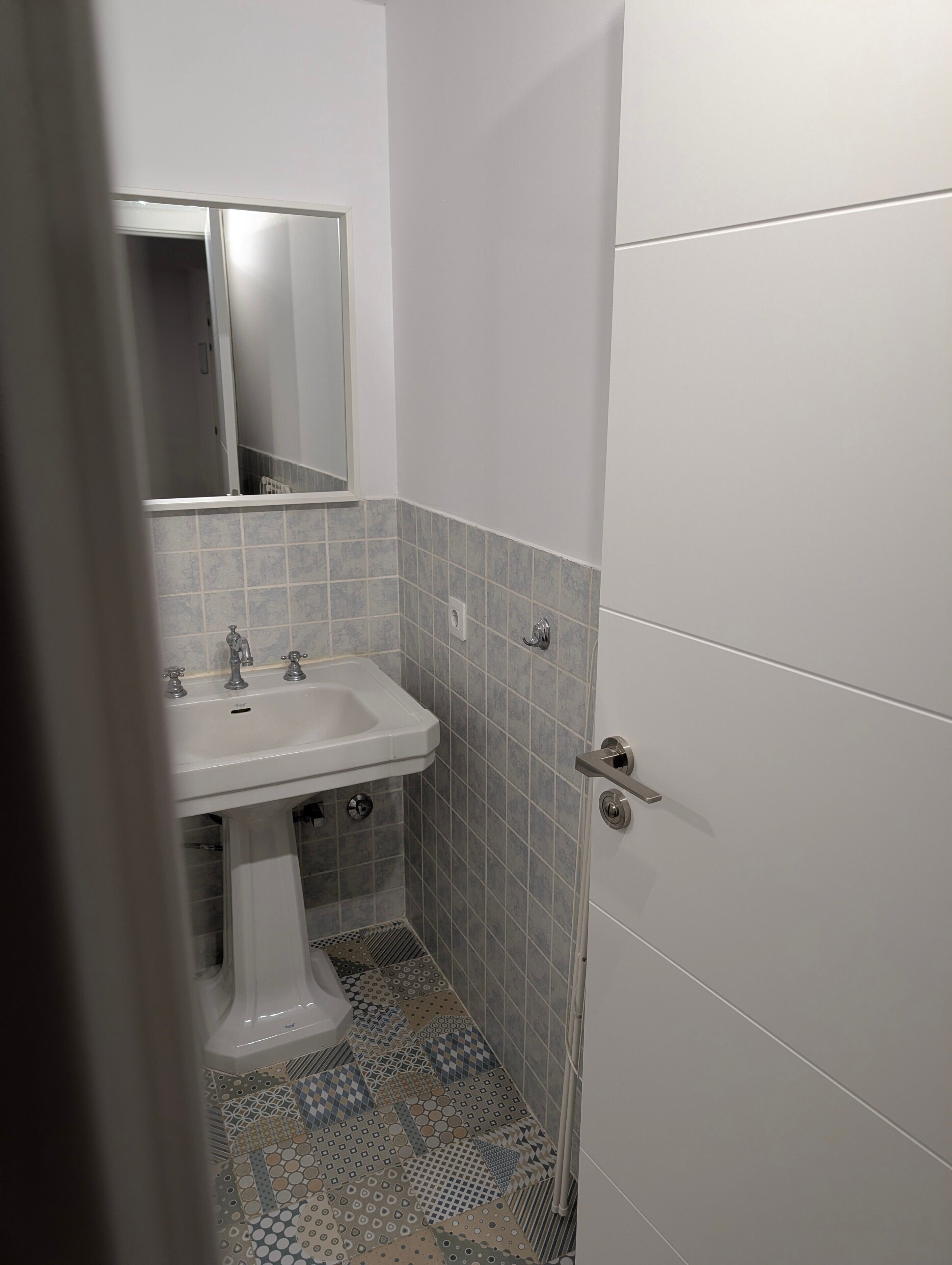 Une salle de bain avec un lavabo blanc, un miroir au-dessus, et un sol carrelé aux motifs variés.