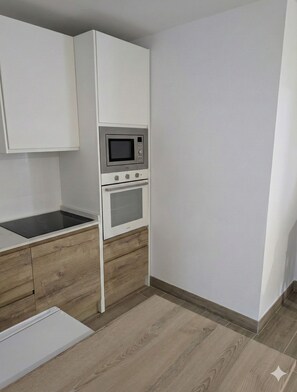 Una cocina compacta con muebles blancos, un microondas y un horno.