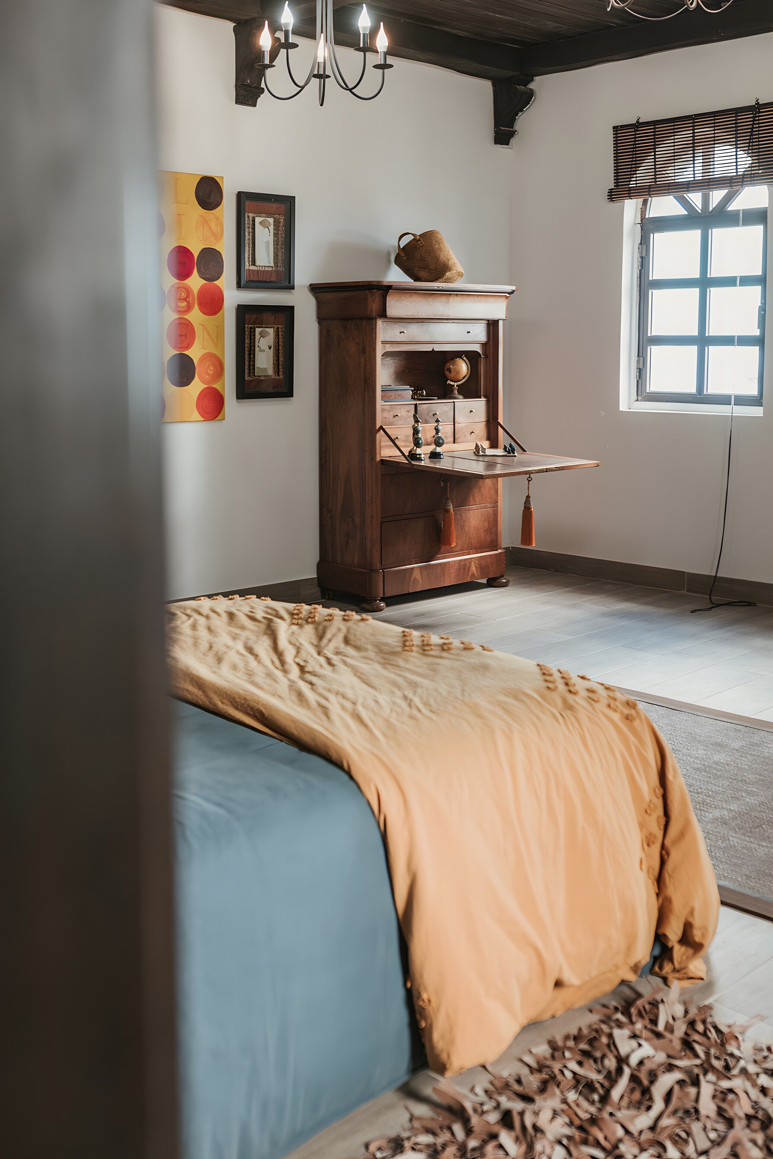 A room with a bed, a wooden cabinet, a chandelier, and artwork on the wall.