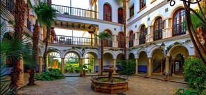 Une cour avec une fontaine, des arcades et des plantes en pot.