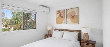 Un dormitorio con cama, dos mesitas de noche, ventilador de techo y una obra de arte en la pared.