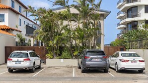 Un parking avec trois voitures, un immeuble doté de balcons et des palmiers.