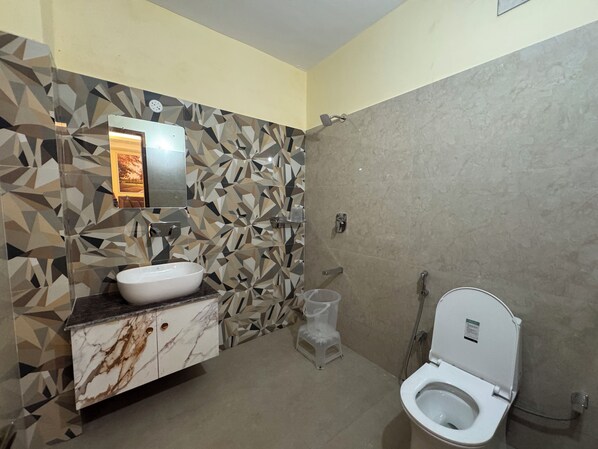 A bathroom with a marble vanity, a wall-mounted mirror, a toilet, and a shower. - HOTEL SHIWALIK GRAND (Haridwar)