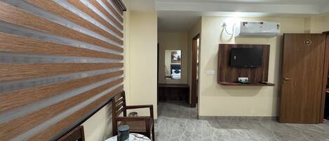 A hotel room with a wooden slatted wall, a round table with a chair, a bed, a television mounted on the wall, and a door with the number 107.