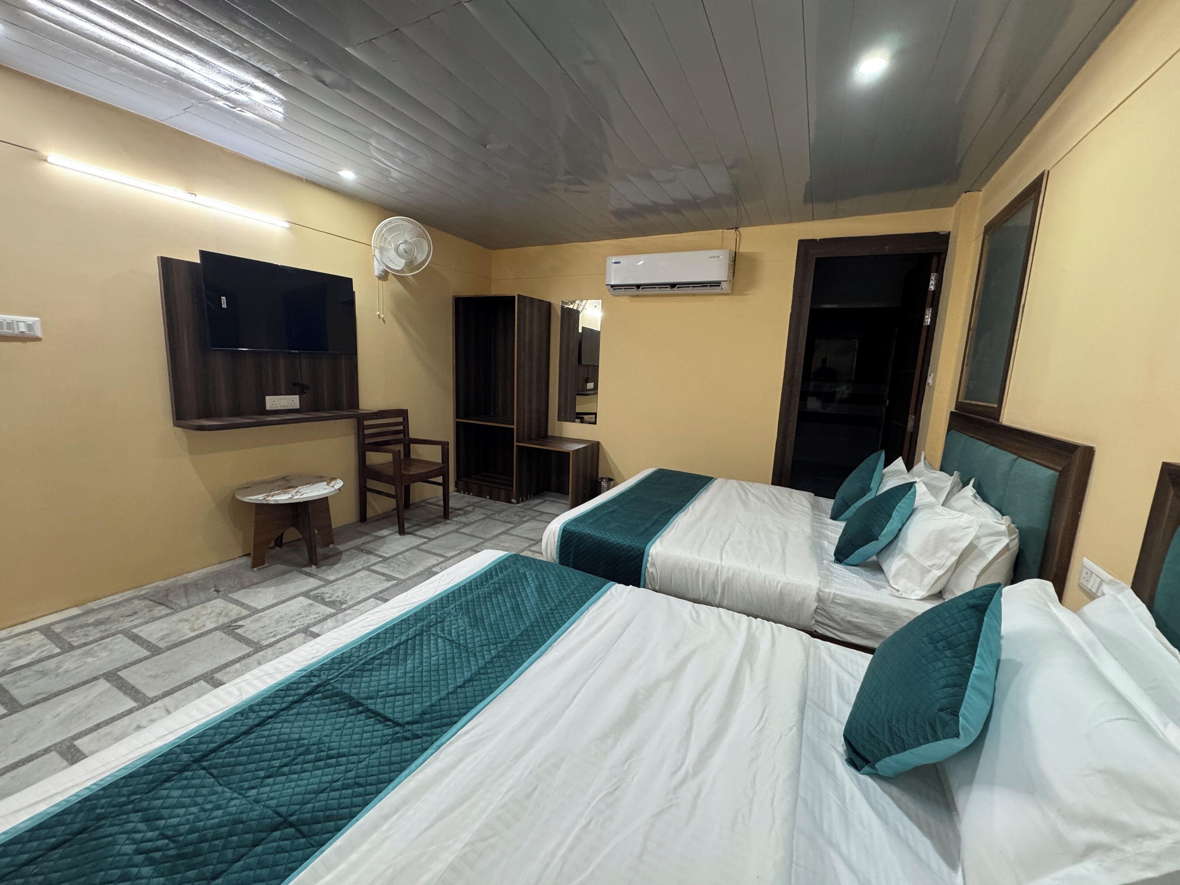 Een hotelkamer met twee bedden, een bureau, een stoel, een televisie en een airconditioning.