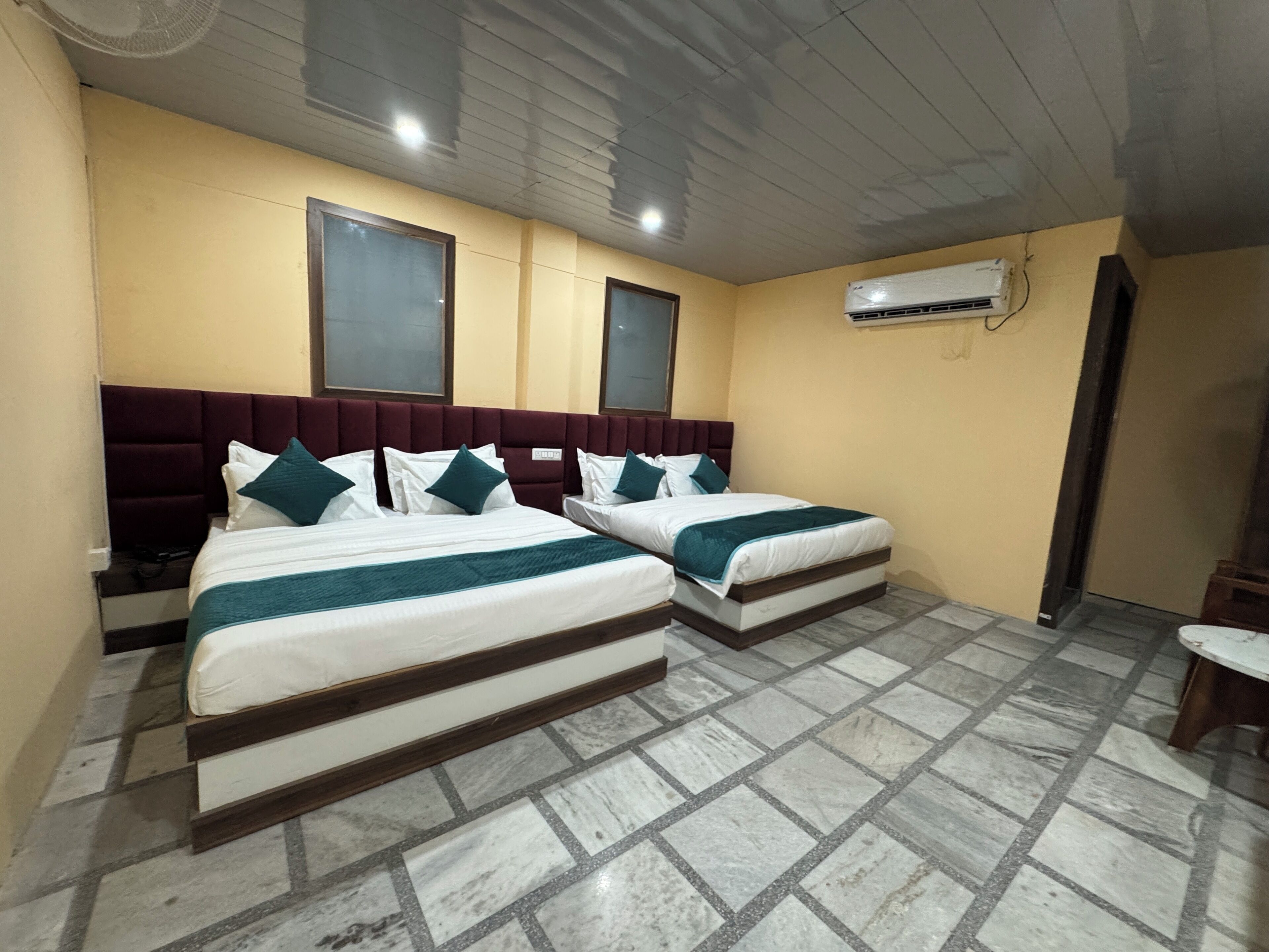 A hotel room with two beds, a ceiling fan, an air conditioning unit, and a tiled floor.