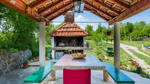 Une terrasse extérieure avec un barbecue en briques, une table avec un saladier et une chaise rouge.
