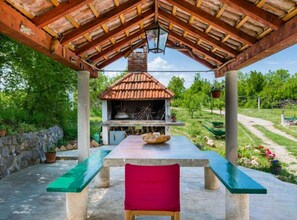 Patio esterno con barbecue in mattoni, tavolo con una ciotola e una sedia rossa.