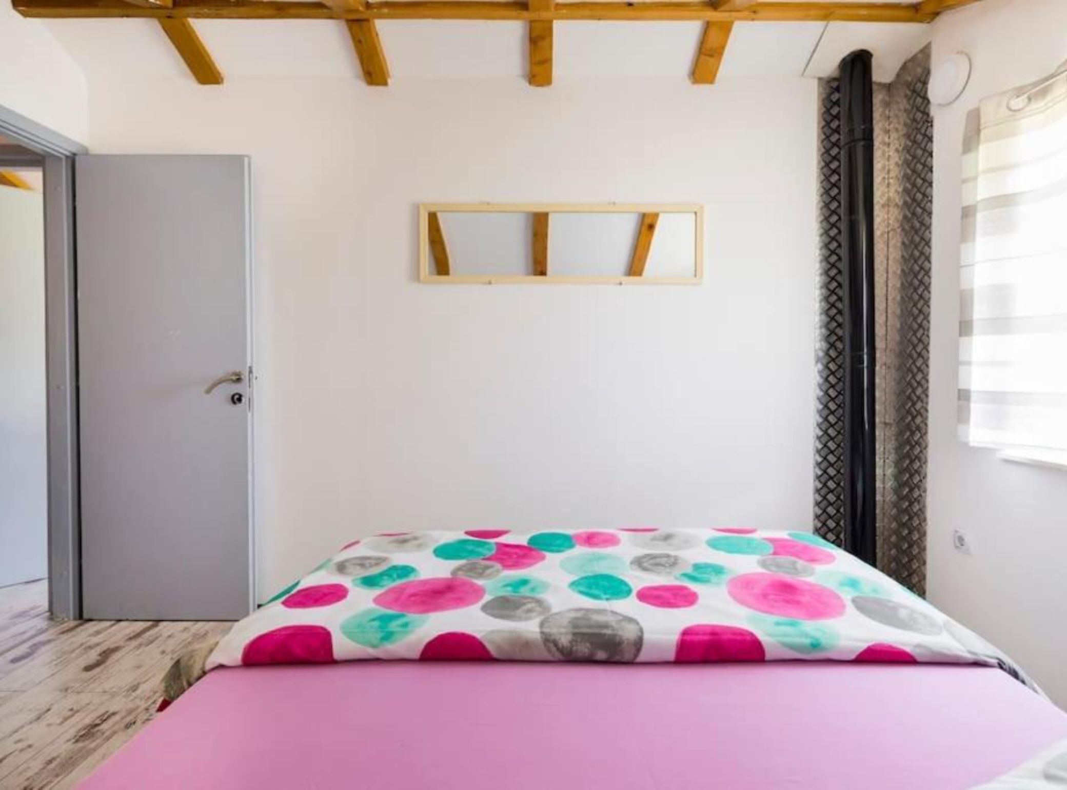 Ein Schlafzimmer mit einem Bett, einer Tür, einem Fenster mit Vorhängen und einer Holzzieldecke.
