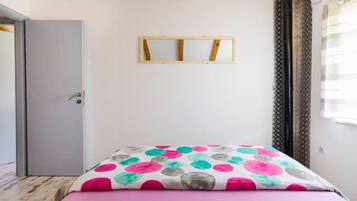Ein Schlafzimmer mit einem Bett, einer Tür, einem Fenster mit Vorhängen und einer Holzzieldecke.