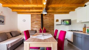 Un salon chaleureux avec un plafond en bois, un mur d’accent en briques, une table à manger avec des chaises et un coin cuisine équipé de placards et d’une cuisinière.