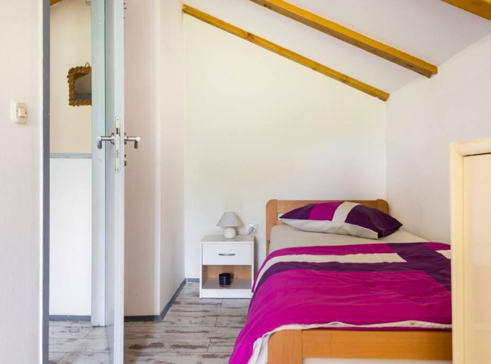 Une chambre à coucher comprenant un lit, une table de chevet, une lampe et une porte donnant sur une autre pièce.