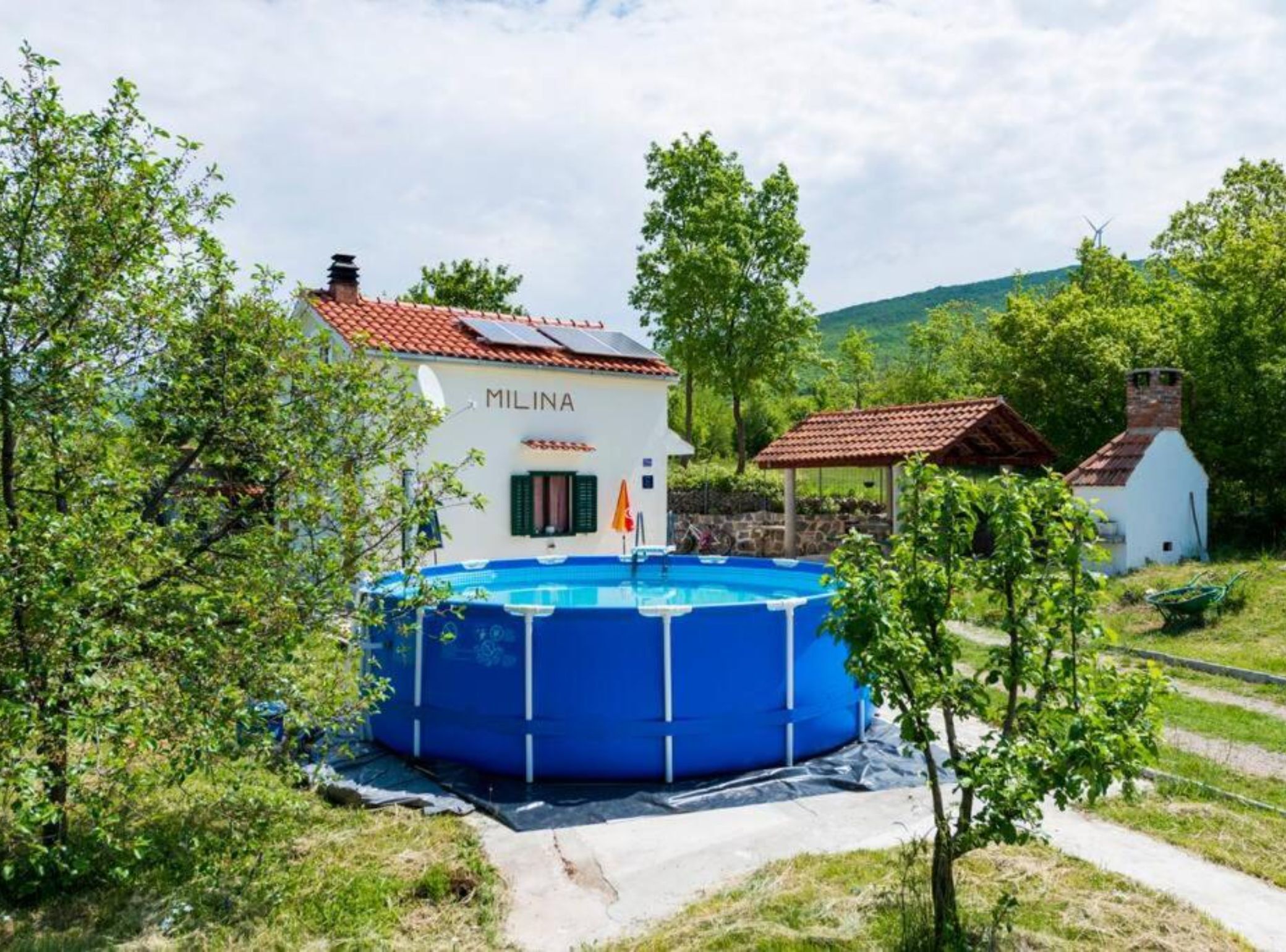 A white building with a red roof labeled "MILINA" and a blue above-ground pool.