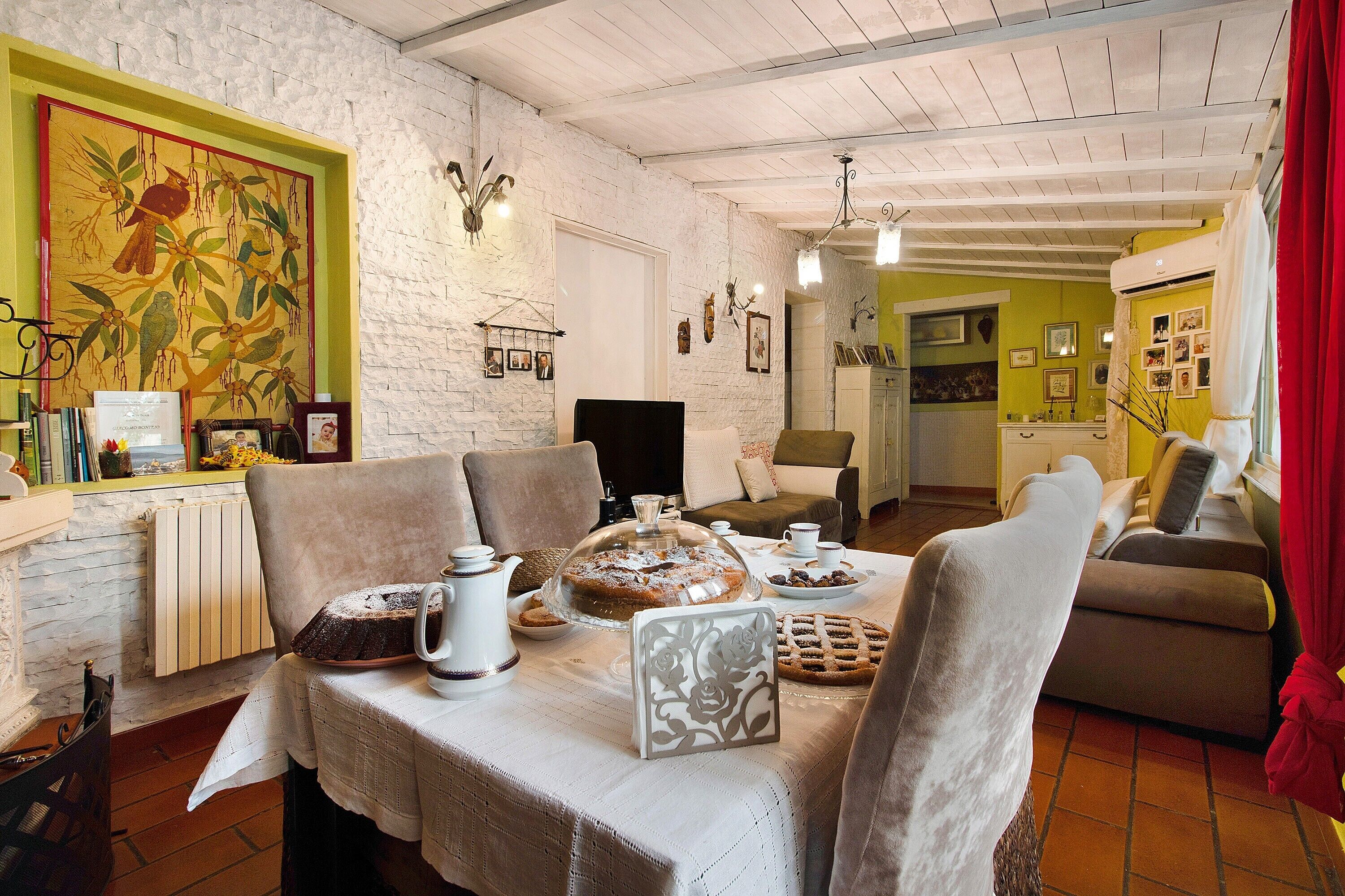 Un'area pranzo con tavolo apparecchiato, sedie, un termosifone e una parete con quadri.