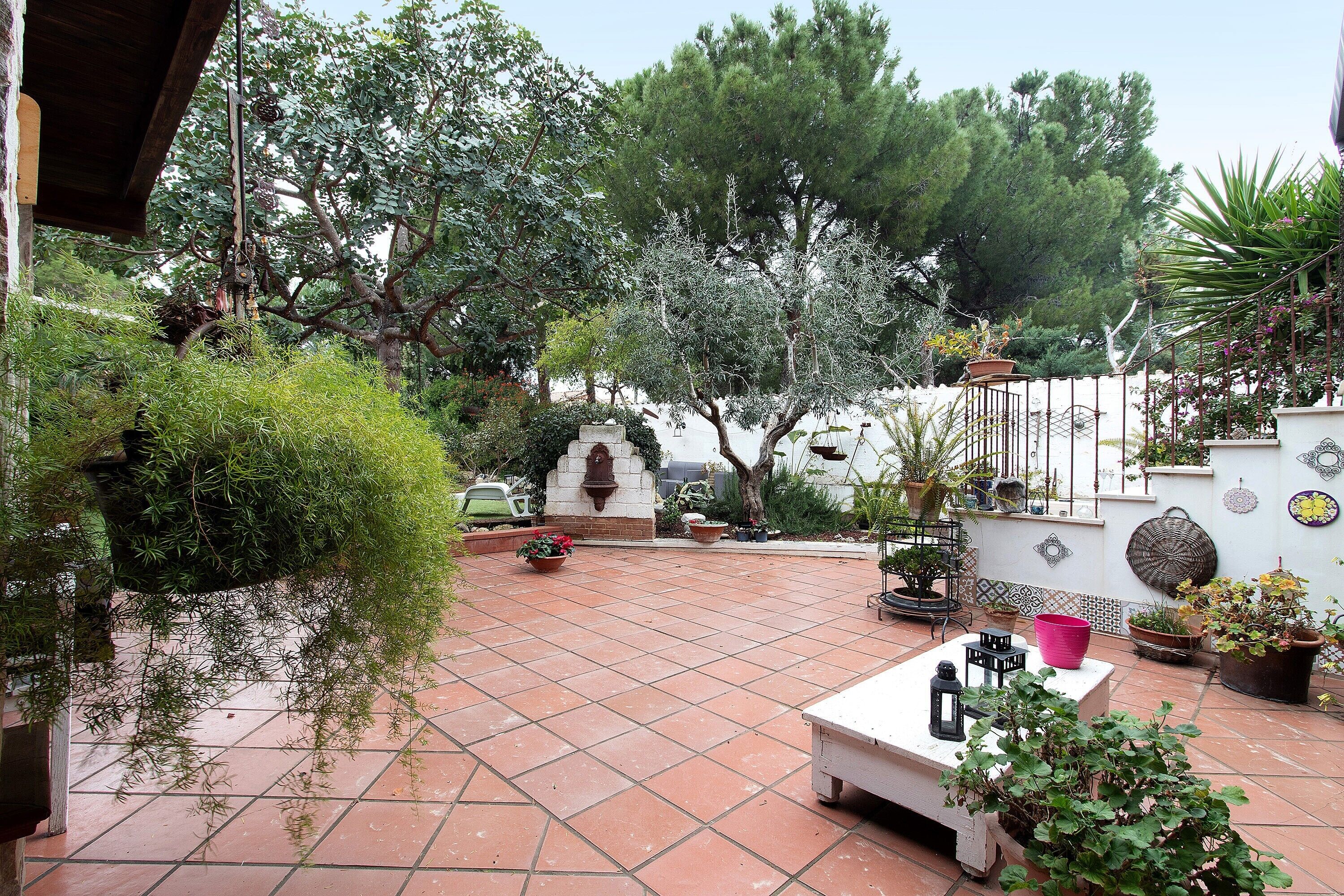 Une cour avec un sol carrelé, des plantes en pot, une table blanche et un mur décoratif.