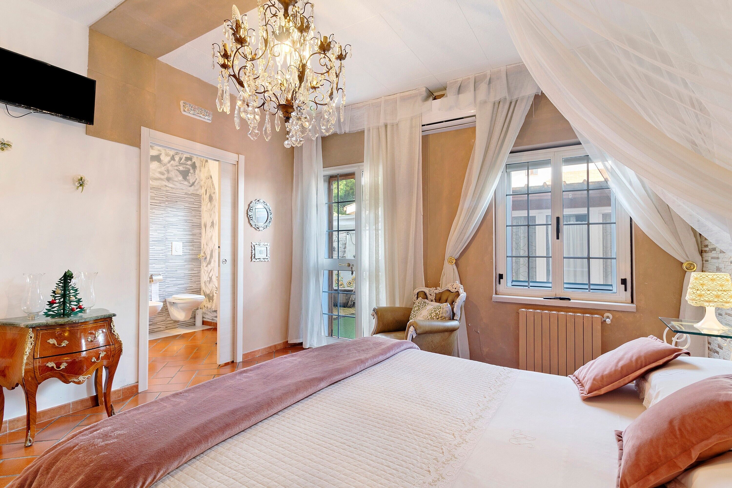 A bedroom with a bed, a chandelier, a window with curtains, a radiator, and a wooden dresser.